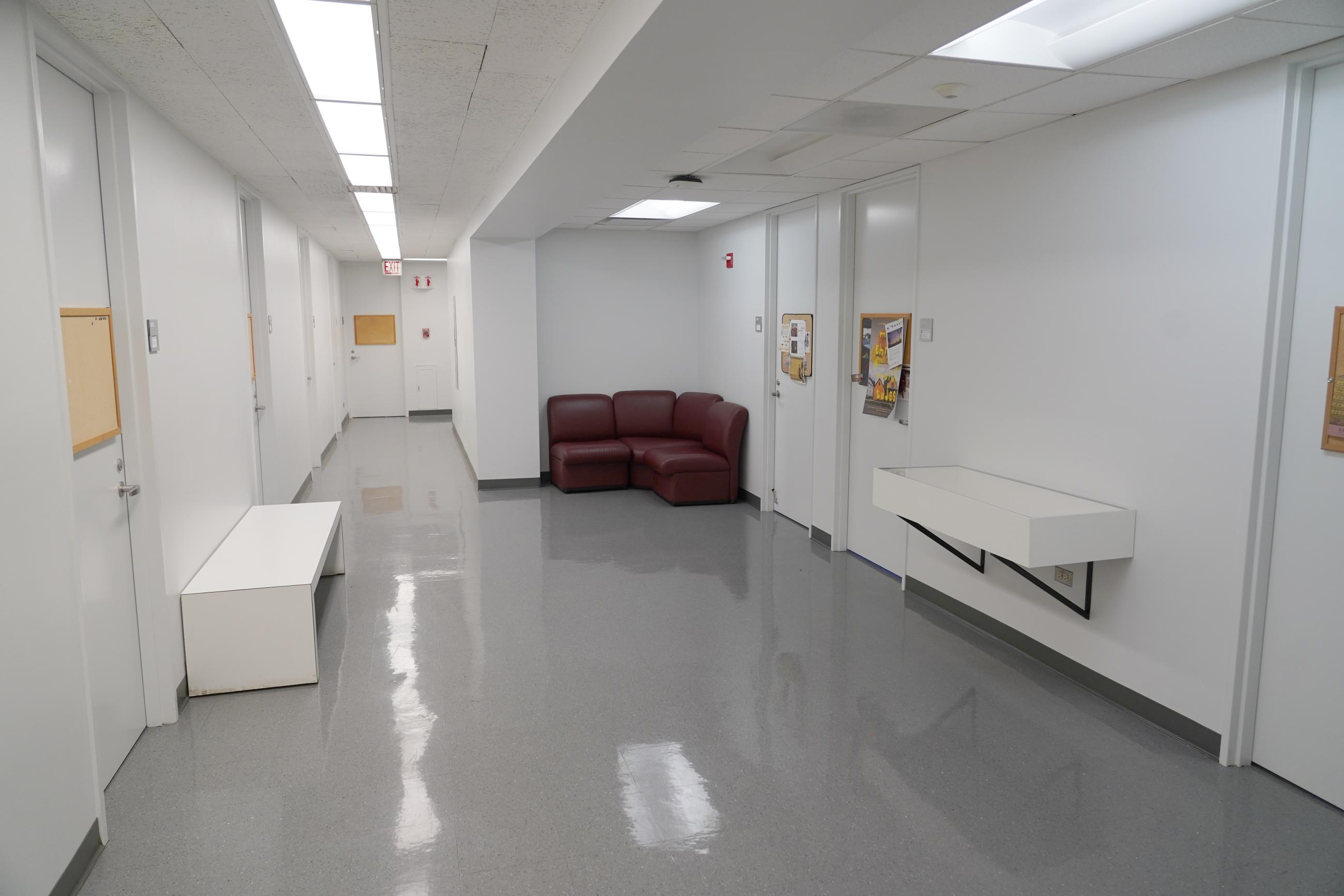 View of CWAC hallway with display case at right between two offices, bench at left