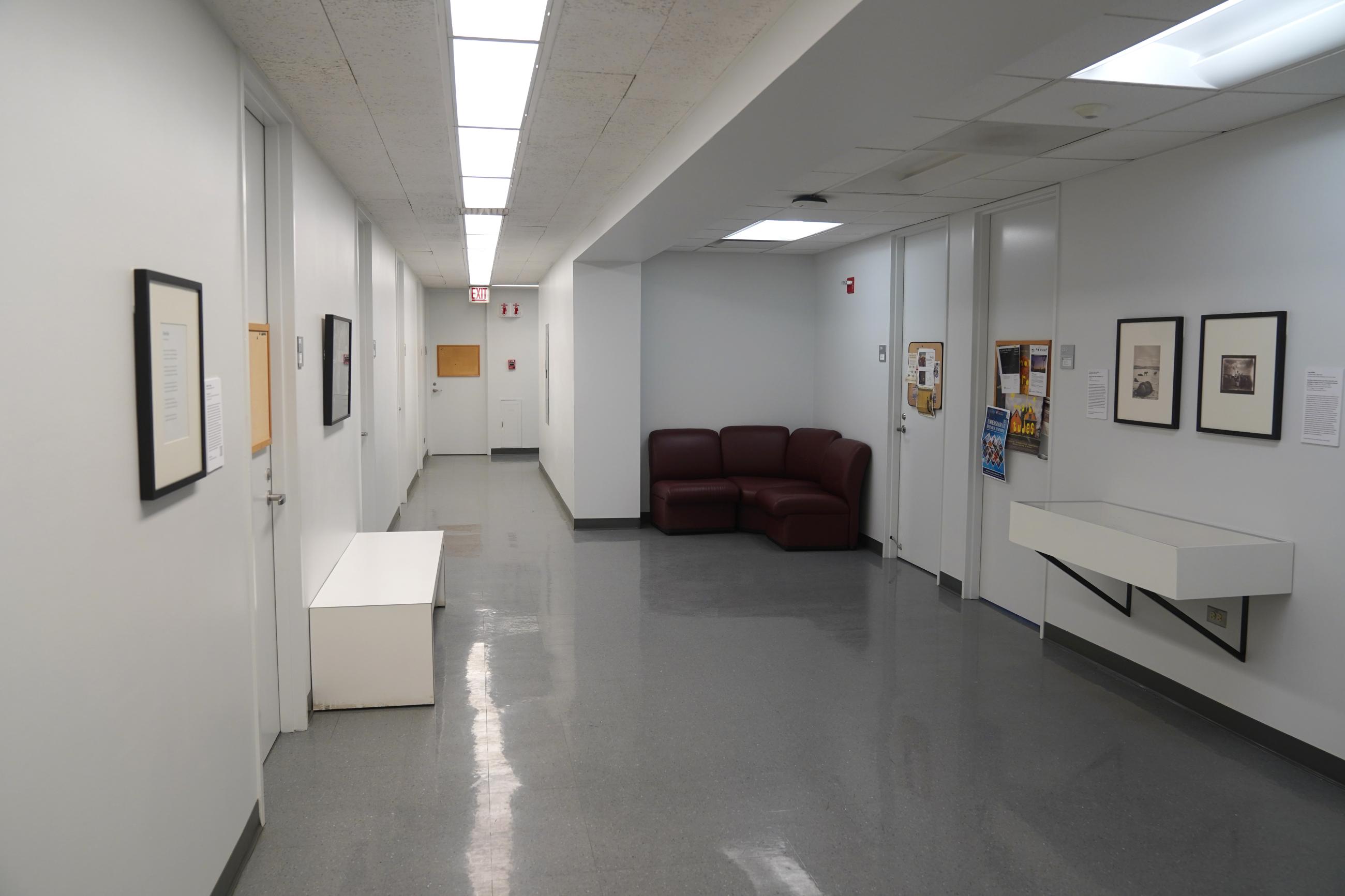 View of white hallway with framed works on wall and an object case 