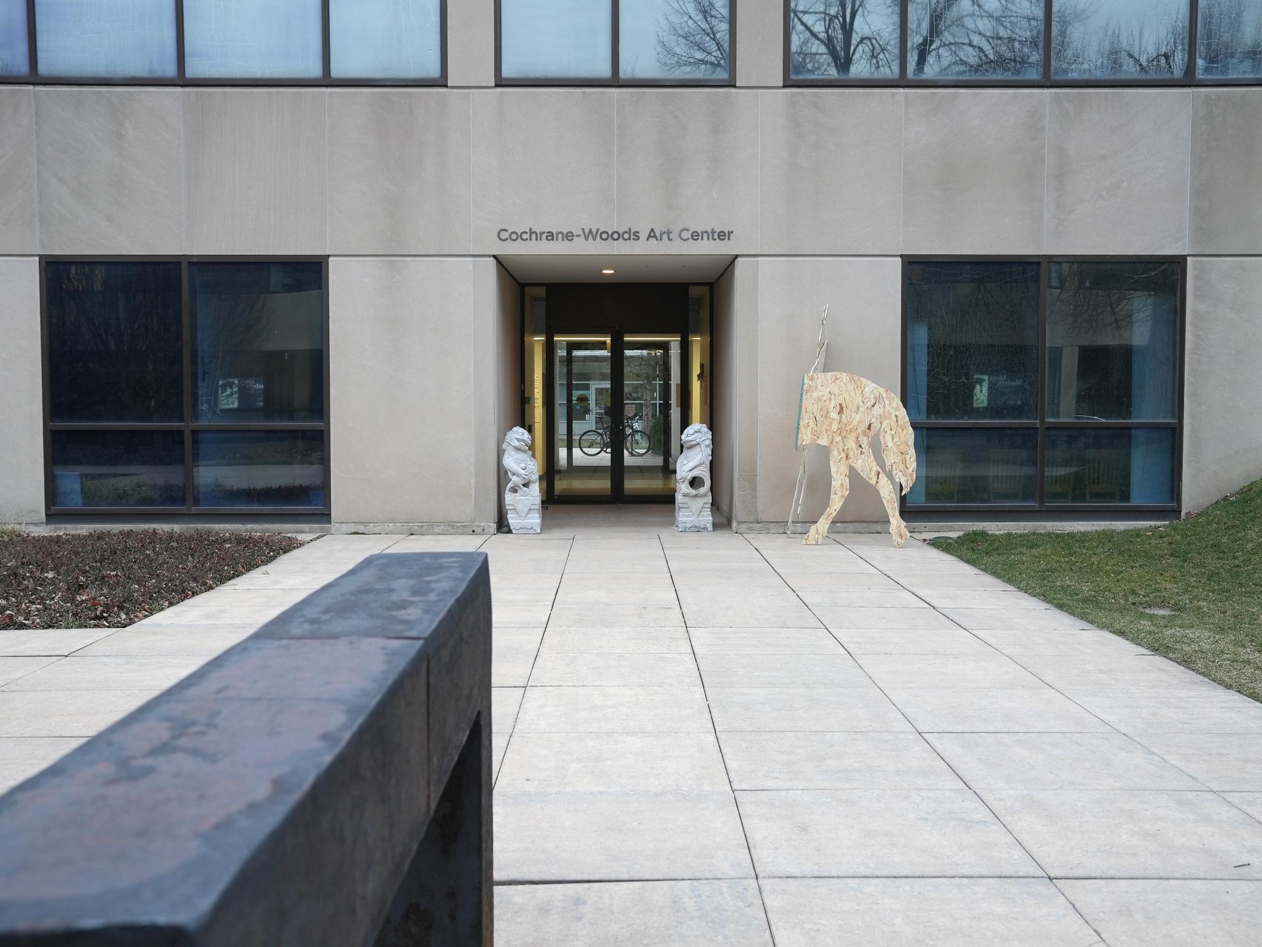 life-size silhouettes of horses made from plywood, hinged, outside of building with two stone dragons flanking entryway