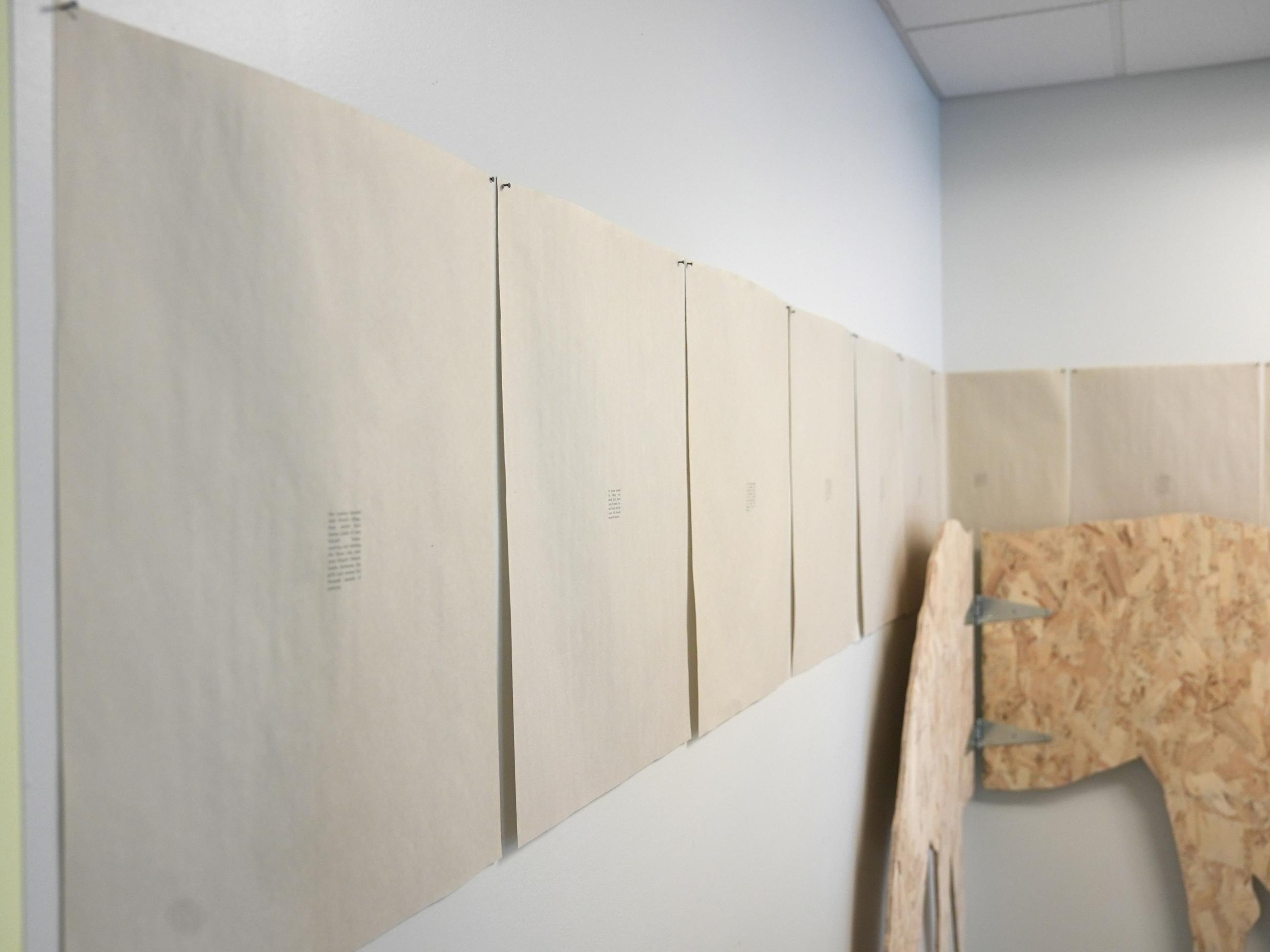 life-size silhouettes of horses made from plywood, hinged, with printed text on paper lined up on wall