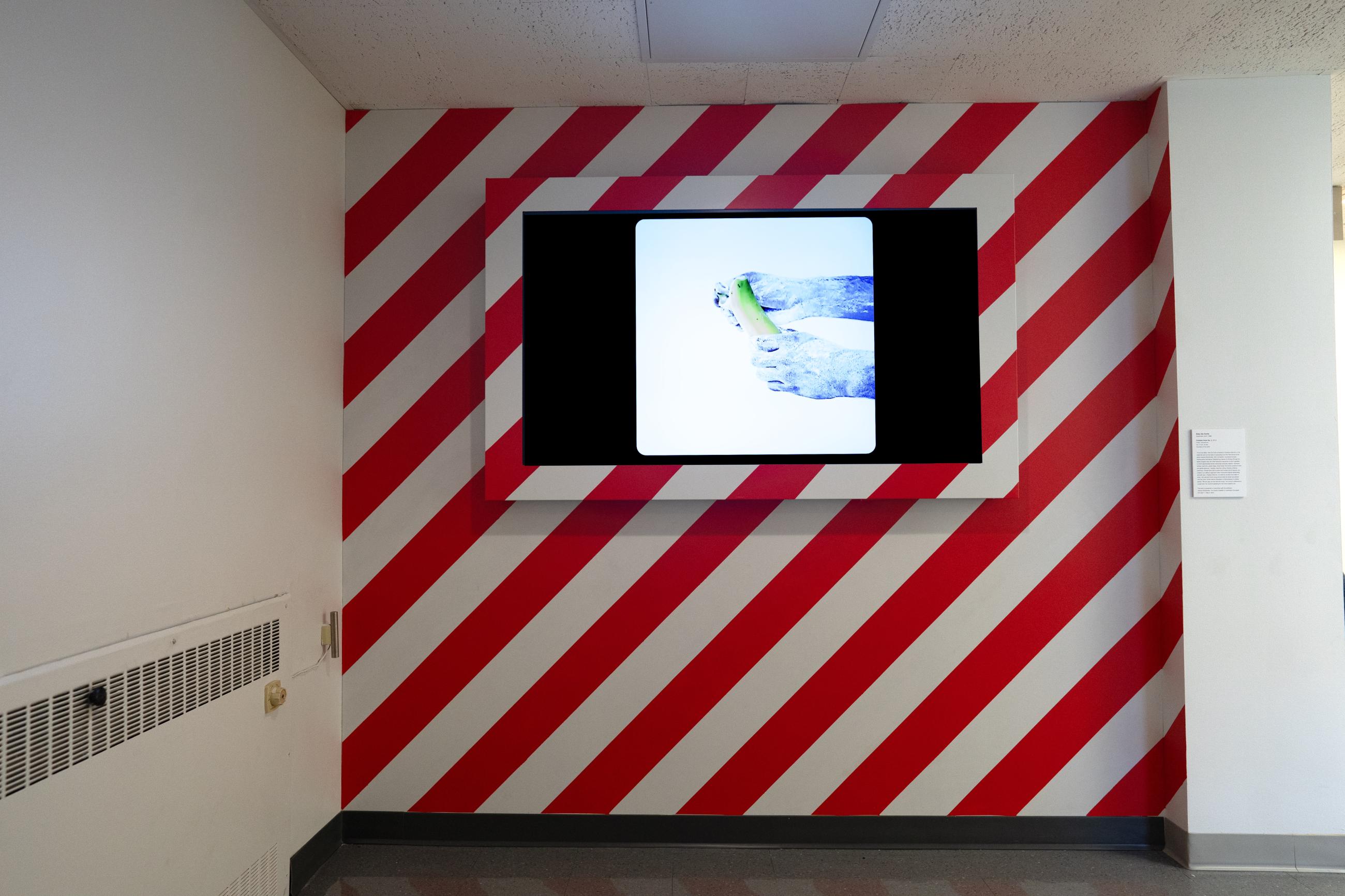A monitor playing an art video on a diagonally striped red and white wall