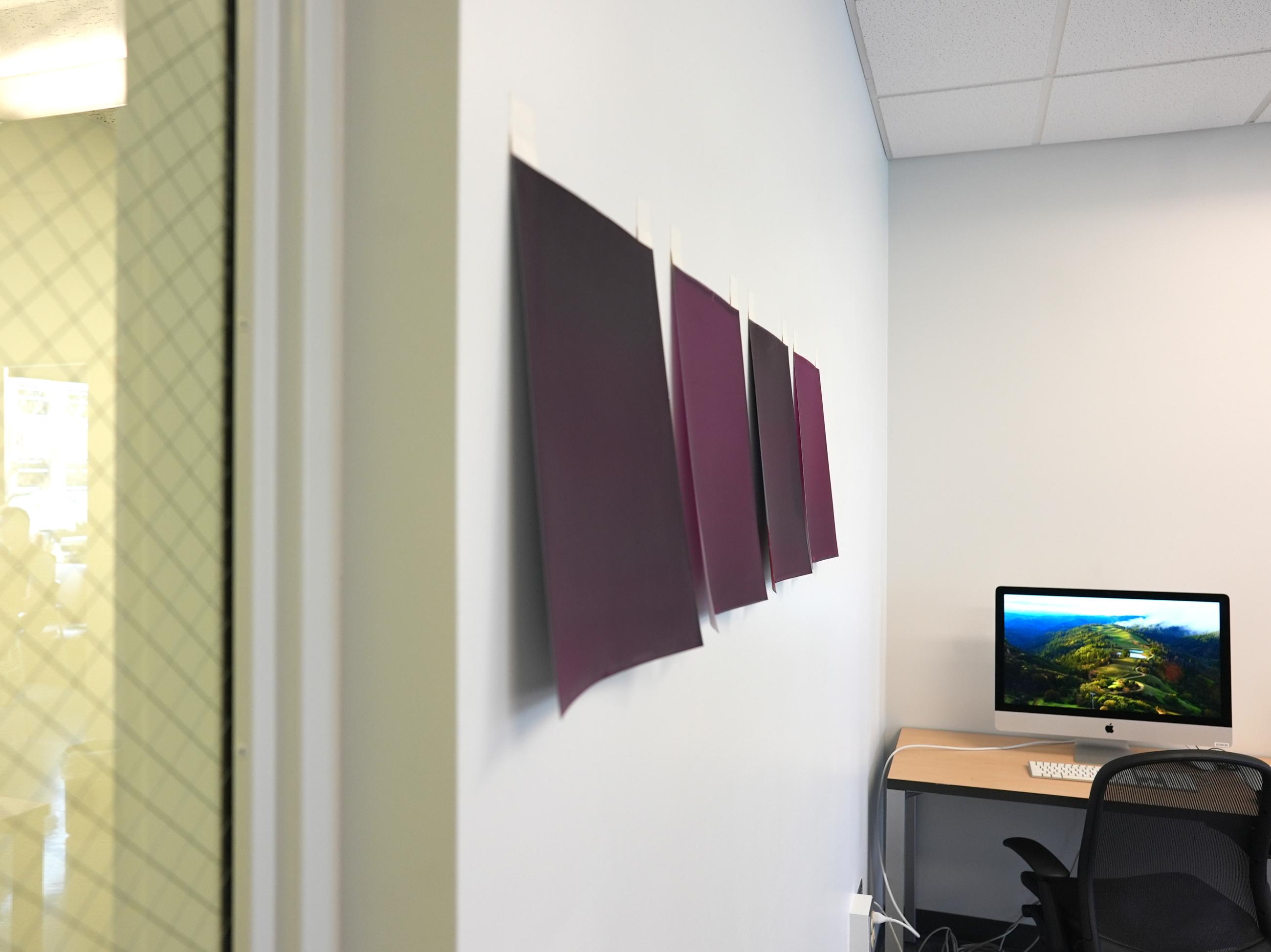 Side view of four letter-sized paintings of solid purple hung on a white wall