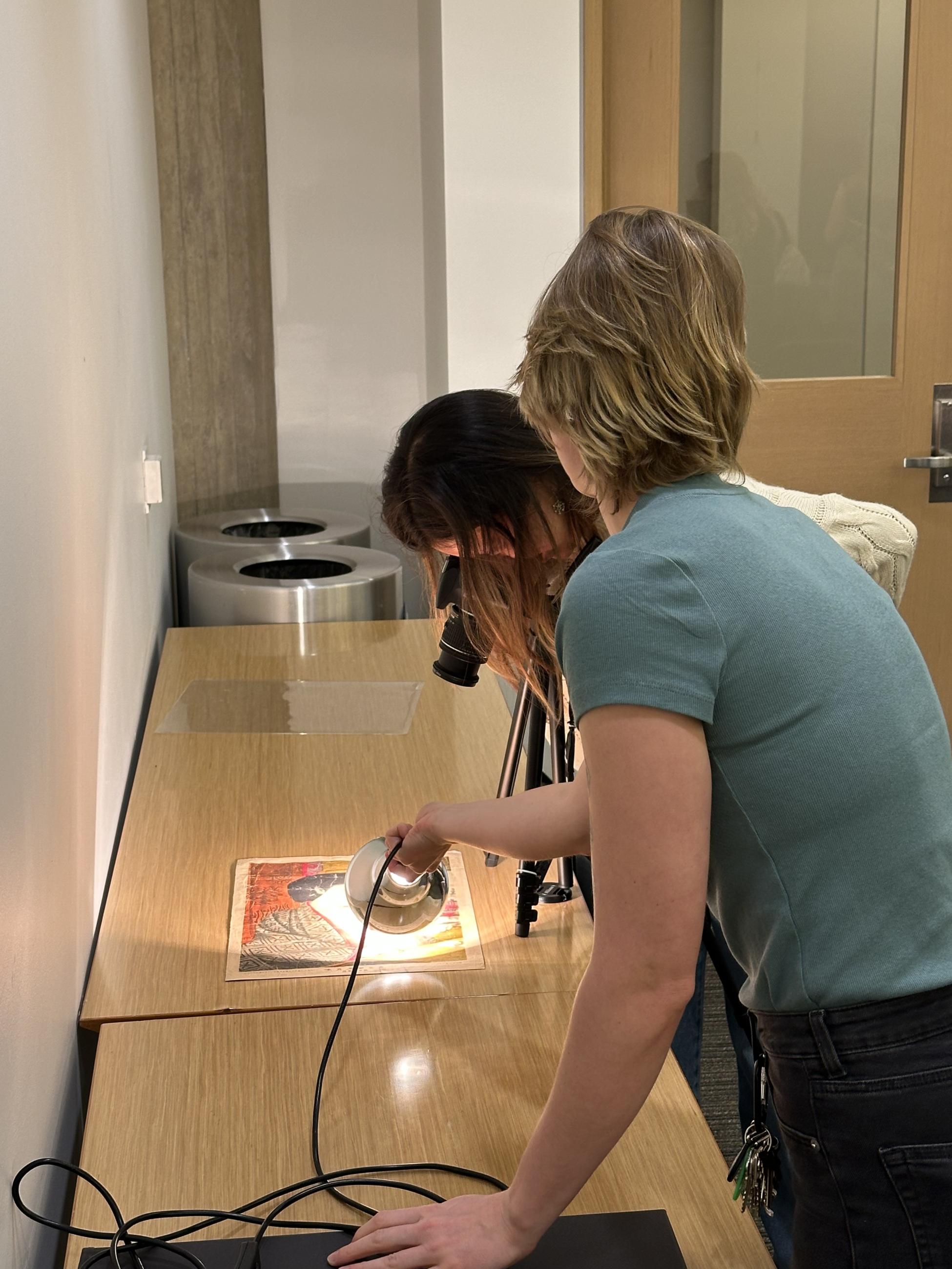 Two people holding a lamp to a print