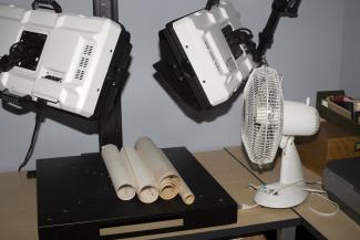 Rolls of paper on a stand underneath two high tech lights, with a white stand fan