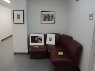 Framed works of art, some hanging on a white wall, others resting on a maroon couch awaiting installation